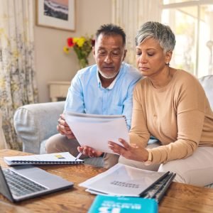 Laptop, documents and finance with a senior couple in the home living room for retirement or budget planning. Computer, accounting or investment savings with a mature man and woman in a house.